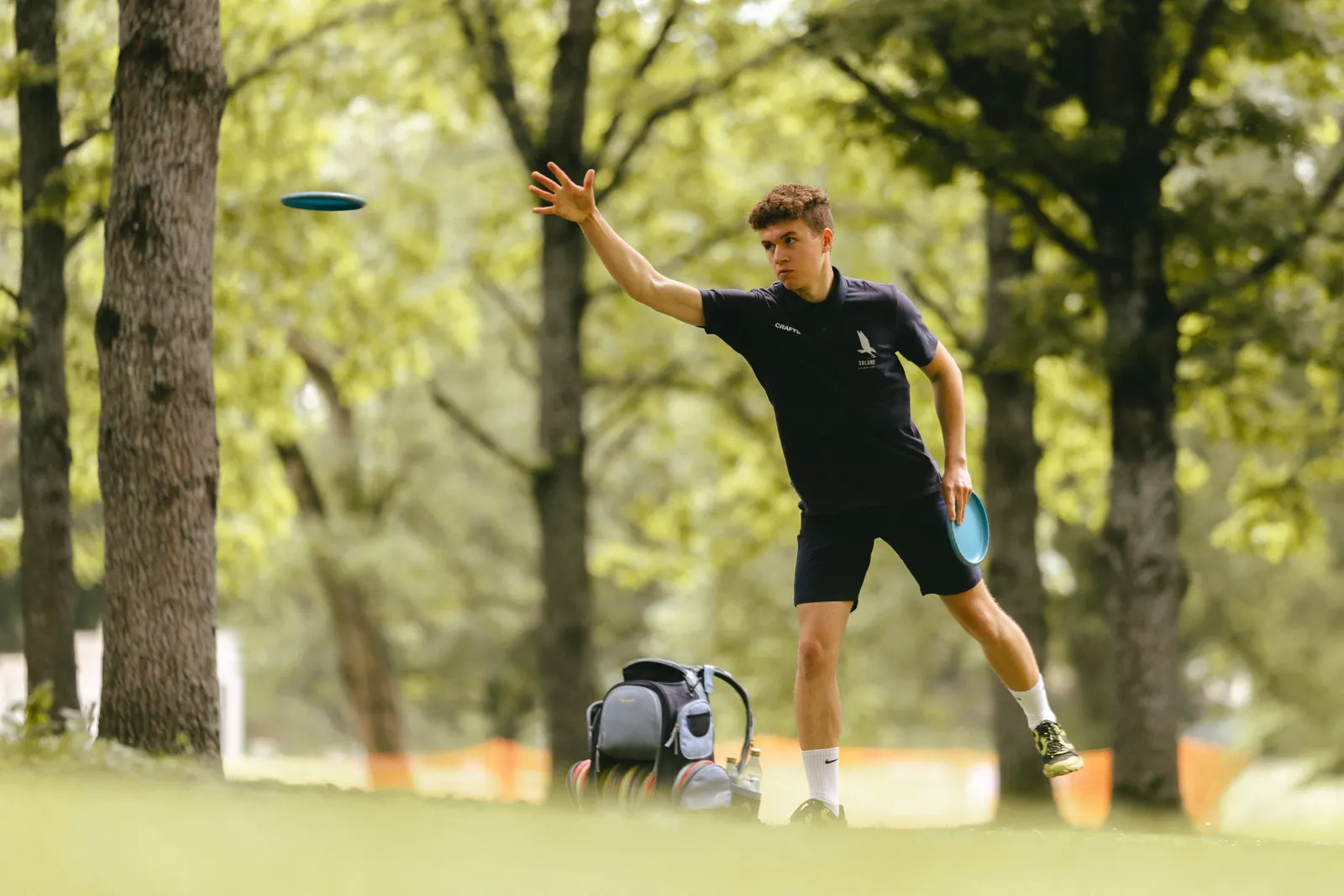 Player releasing a drive among the trees, disc in the air